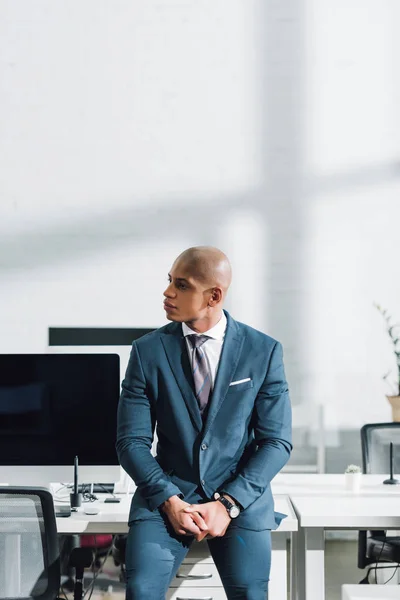 Молодий афроамериканець бізнесмен дивитися вбік, сидячи в офісі — стокове фото