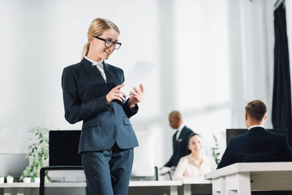 Sonriente joven mujer de negocios en gafas usando tableta digital en la oficina - foto de stock