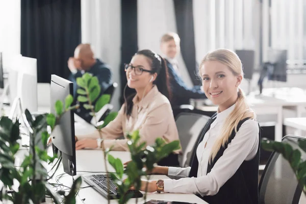 Lächelnde junge Geschäftsfrauen, die im Großraumbüro mit Computern arbeiten — Stockfoto