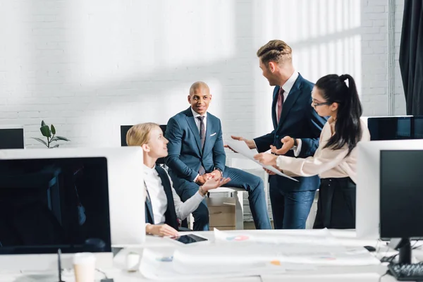 Lächelnde junge multiethnische Geschäftskollegen, die gemeinsam im Büro über ein Projekt diskutieren — Stockfoto