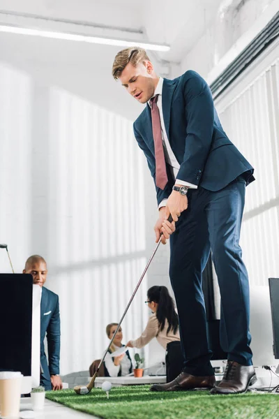 Low angle view of young businessman playing golf in office — Stock Photo