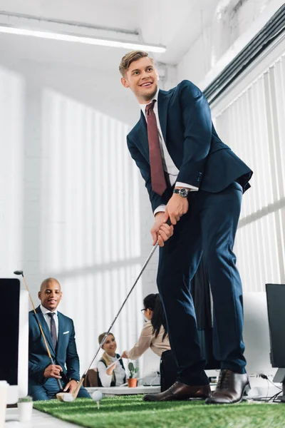 Visão de baixo ângulo de feliz jovem empresário jogando golfe no escritório — Fotografia de Stock