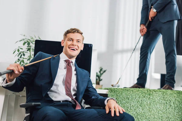 Happy young businessman playing golf with colleague in office — Stock Photo