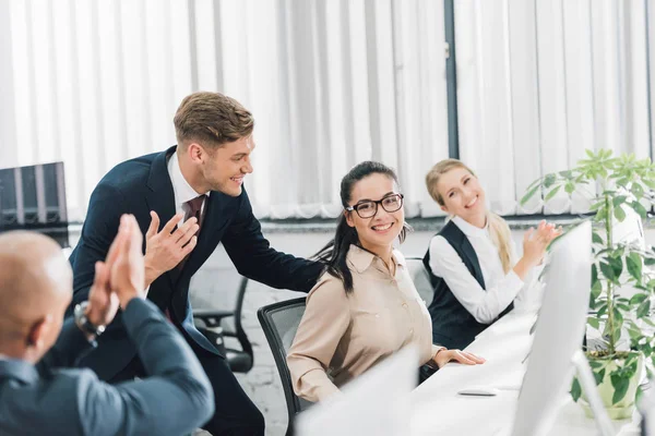 Smiling young coworkers greeting and applauding to happy female colleague in office — Stock Photo