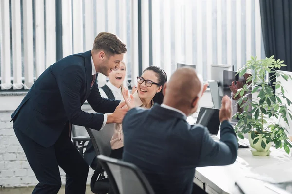 Fröhliche junge Geschäftskollegen lachen und applaudieren am Arbeitsplatz — Stockfoto