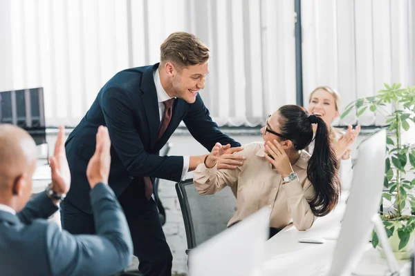 Cheerful young business people greeting happy female colleague at workplace — Stock Photo