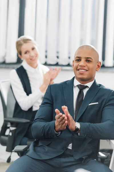 Sonriendo jóvenes empresarios multiétnicos aplaudiendo en el lugar de trabajo - foto de stock