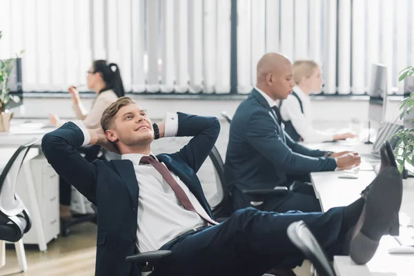 Giovane uomo d'affari sorridente seduto con le mani dietro la testa e guardando in alto in ufficio — Foto stock
