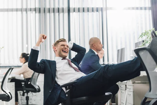 Aufgeregter junger Geschäftsmann triumphiert bei der Arbeit mit Kollegen im Großraumbüro — Stockfoto