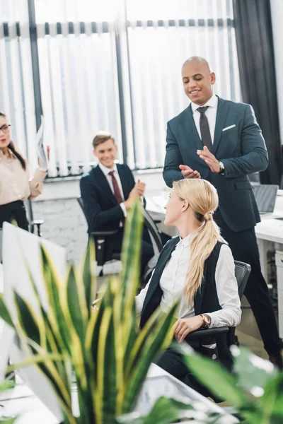 Feliz joven colegas aplaudiendo a sonriente mujer de negocios en el cargo - foto de stock