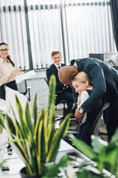 Happy young african american businessman hugging smiling female colleague in office — Stock Photo