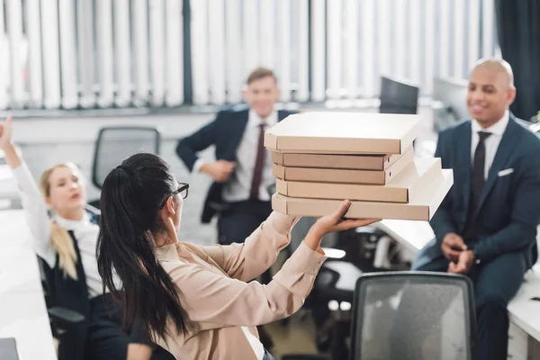 Junge Geschäftsfrau zeigt glücklichen Kollegen im Großraumbüro Pizzakartons — Stockfoto