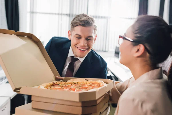 Giovane donna d'affari che tiene scatole di pizza e uomo d'affari sorridente guardando gustosa pizza — Foto stock