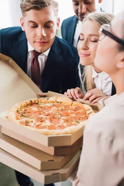 Plan recadré de jeunes collègues d'affaires sentant la pizza savoureuse au bureau — Photo de stock
