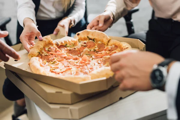 Primer plano vista parcial de compañeros de trabajo comiendo pizza en la oficina - foto de stock