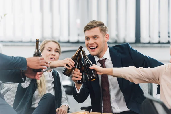 Plan recadré de jeunes collègues heureux clinquant bouteilles de bière au bureau — Photo de stock