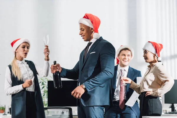 Felizes jovens colegas de negócios multirraciais em chapéus de santa celebrando o Natal no escritório — Fotografia de Stock