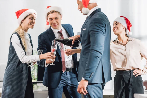 Heureux jeunes collègues multiraciaux d'affaires dans santa chapeaux célébrer la nouvelle année au bureau — Photo de stock