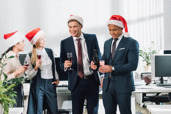 Happy young multiracial coworkers in santa hats celebrating new year in office — Stock Photo