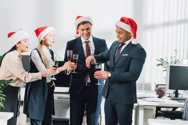 Fröhliche junge multiethnische Mitarbeiter in Weihnachtsmänteln feiern Weihnachten im Büro — Stockfoto