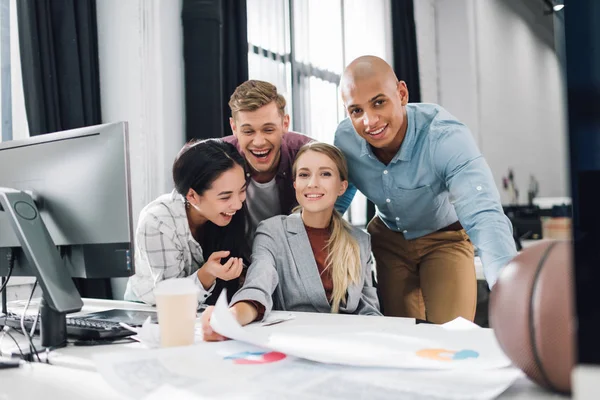 Heureux jeunes collègues multiraciaux d'affaires souriant à la caméra tout en travaillant ensemble dans le bureau — Photo de stock