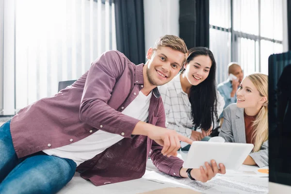 Jóvenes empresarios felices utilizando tableta digital y sonriendo en la oficina de espacio abierto - foto de stock