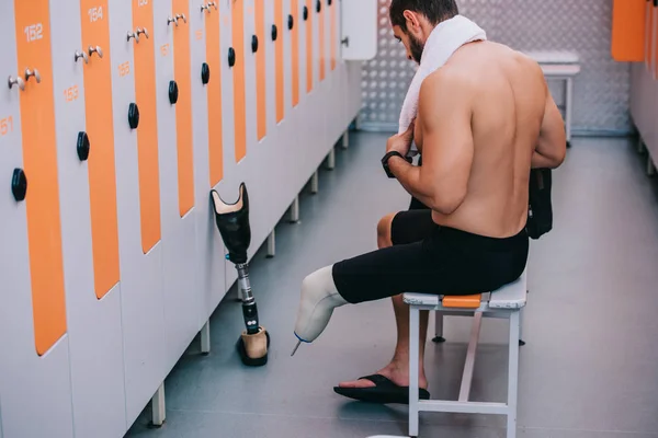 Atlético joven deportista con pierna artificial sentado en el banco en el vestuario de la piscina - foto de stock