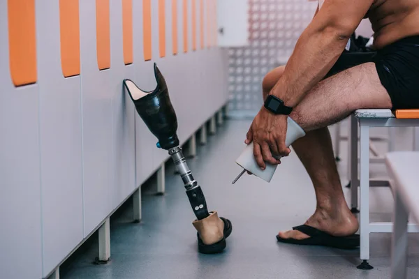 Tiro recortado de deportista con pierna artificial sentado en el banco en el vestuario de la piscina - foto de stock