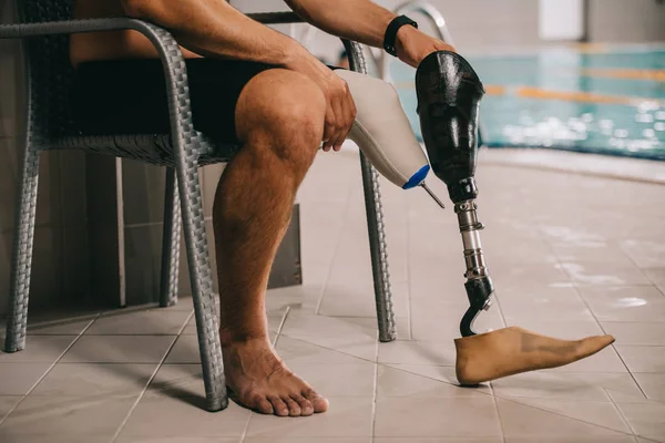 Tiro recortado de deportista con pierna artificial sentado en la silla en la piscina cubierta - foto de stock