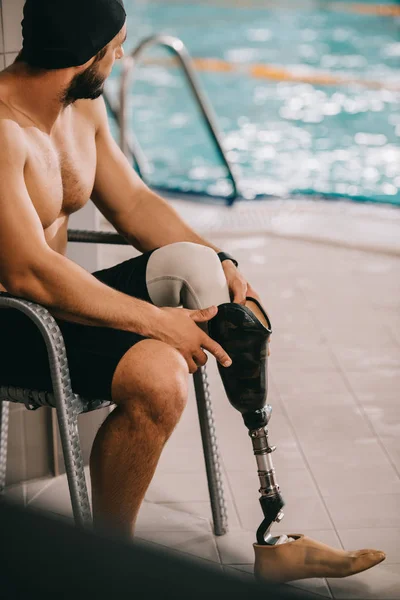 Deportista feliz con pierna artificial sentado en la silla en la piscina cubierta - foto de stock