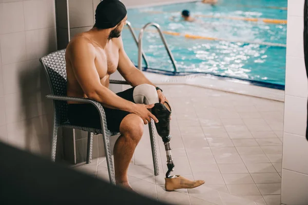 Athletic sportsman with artificial leg sitting on chair at indoor swimming pool — Stock Photo