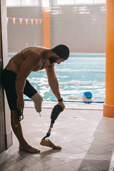 Atlético jovem nadador de pé à beira da piscina interior e decolando perna artificial — Fotografia de Stock