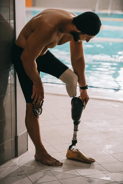 Beau nageur debout au bord de la piscine intérieure et décollant jambe artificielle — Photo de stock