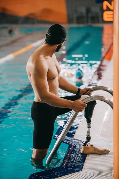 Muskulöser junger Schwimmer mit künstlichem Bein steigt aus Schwimmbad aus — Stockfoto