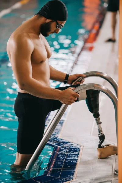 Side view of handsome young swimmer with artificial leg getting out of swimming pool — Stock Photo