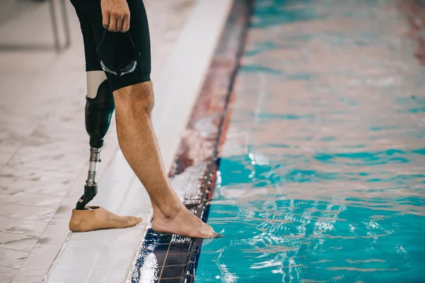 Colpo ritagliato di nuotatore in forma con gamba artificiale in piedi a bordo piscina in piscina coperta e controllo della temperatura dell'acqua — Foto stock