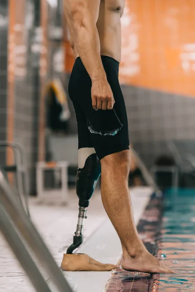 Cropped shot of swimmer with artificial leg standing on poolside at indoor swimming pool and checking water temperature — Stock Photo