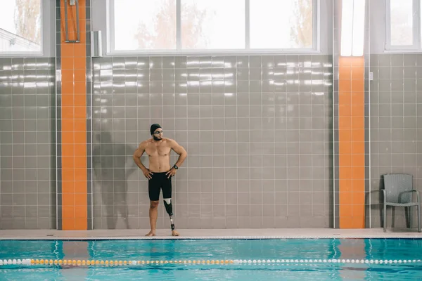 Athletic young sportsman with artificial leg standing on poolside at indoor swimming pool — Stock Photo