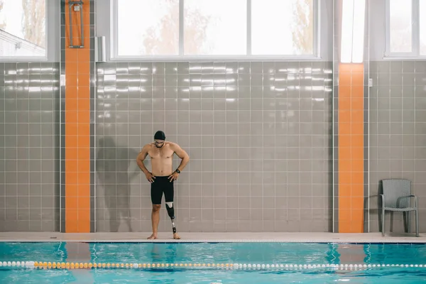 Muskulöser junger Sportler mit künstlichem Bein steht am Beckenrand im Hallenbad — Stock Photo