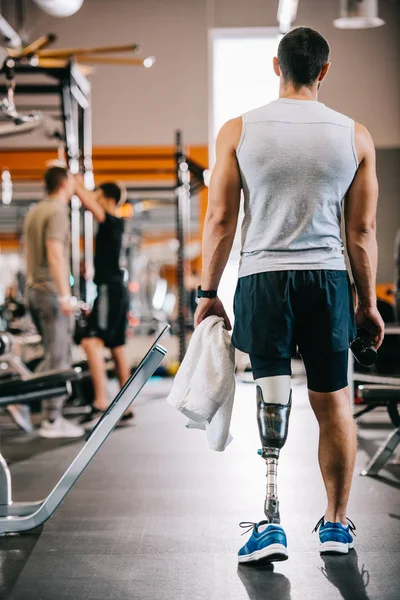 Vista trasera del deportista con pierna artificial de pie en el gimnasio y la celebración de la toalla - foto de stock