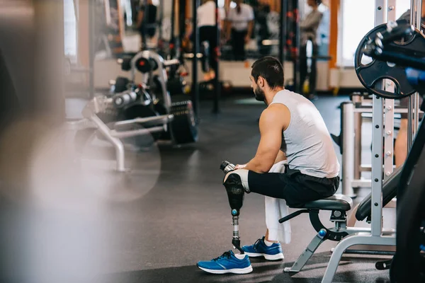 Deportista sobrecargado de trabajo con pierna artificial sentado en el gimnasio - foto de stock