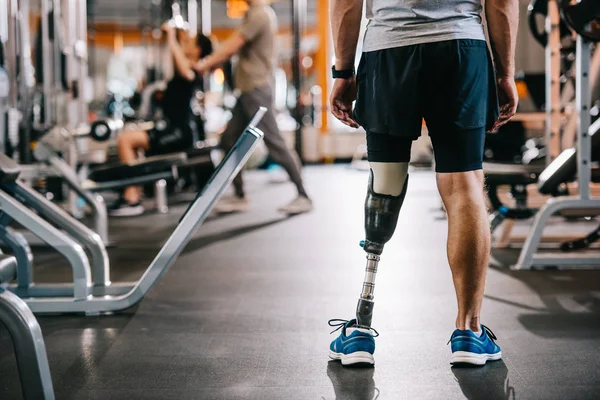 Recortado tiro de de de deportista con pierna artificial de pie en el gimnasio - foto de stock