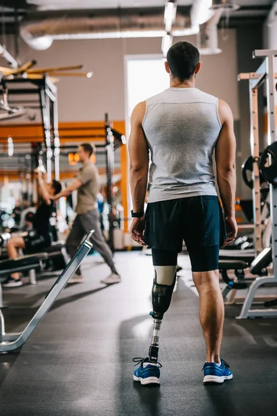 Rear view of sportsman with artificial leg standing at gym — Stock Photo