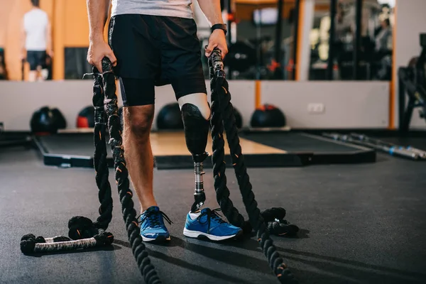 Cropped shot of sportsman with artificial leg working out with ropes at gym — Stock Photo