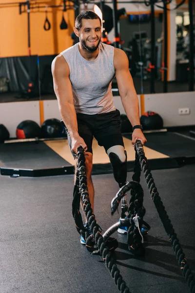 Musculoso joven deportista con pierna artificial haciendo ejercicio con cuerdas en el gimnasio - foto de stock