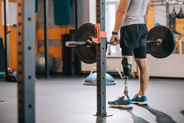 Cropped shot of athletic sportsman with artificial leg working out with barbell at gym — Stock Photo