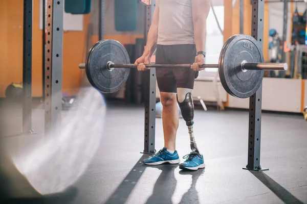 Обрезанный кадр спортсмена с искусственной ногой работает с штангой в тренажерном зале — стоковое фото
