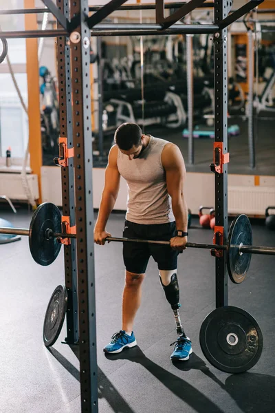 Athletic young sportsman with artificial leg working out with barbell at gym — Stock Photo