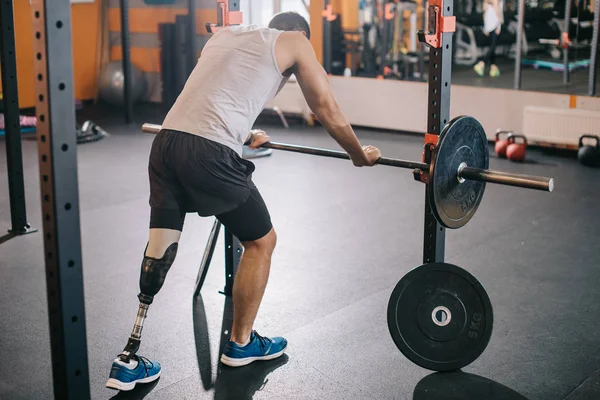 Beau jeune sportif avec jambe artificielle appuyé sur haltère à la salle de gym — Photo de stock