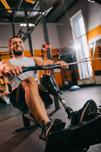 Giovane sportivo muscoloso con gamba artificiale che lavora con vogatore in palestra — Foto stock
